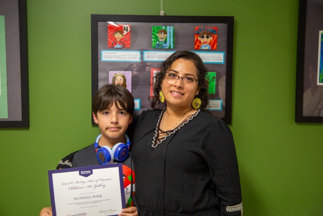 Child posing in front of artwork with art teacher.