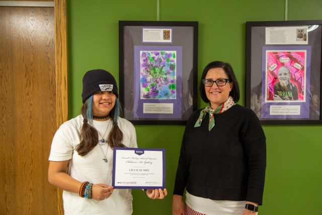 Child posing in front of artwork with art teacher.