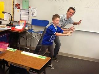man and boy pretending to push a boulder in a classroom