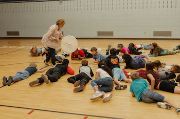 Children laying on ground while teacher plays a drum