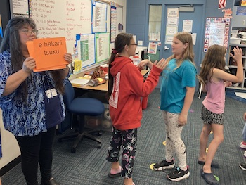 Instructor holding up a sign with a Goshute Greeting and students in partnerships making the associated handshake.