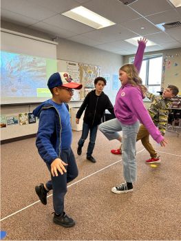 Four students standing on one foot, balancing, and spreading their arms wide, all in different poses.