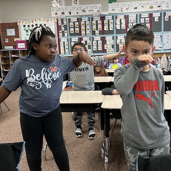 Three elementary school students holding poses like an eagle