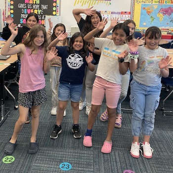 Eight students smiling and waving with both hands towards the camera