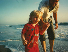 boy walking with help from a man on a beach