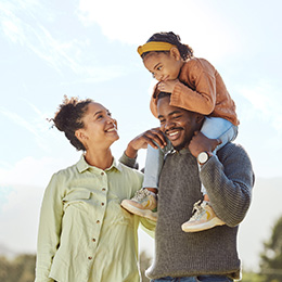 Mother and father stand with daughter on his shoulders