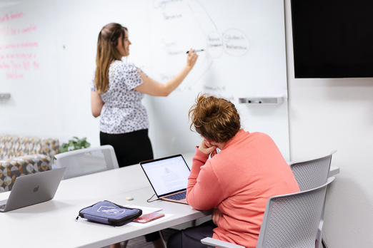 Woman writing at a whiteboard with another woman watching