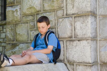 boy sitting by a wall while wearing a backpack