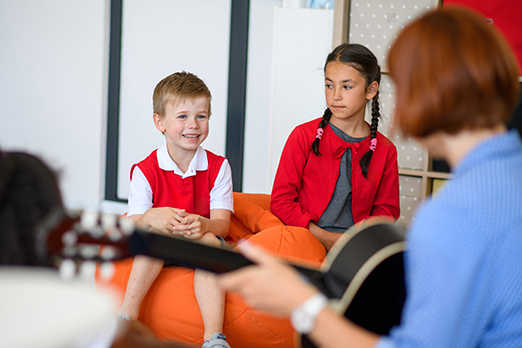 students smile as a teacher plays guitar