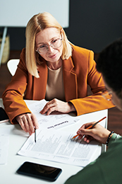 a woman in an orange suit jacket assists a coworker