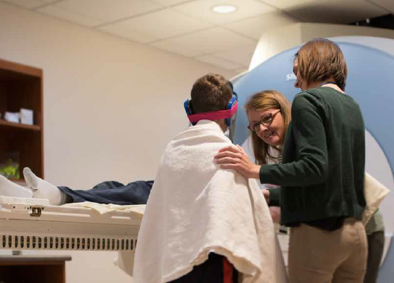 A woman and boy talk to a doctor in front of an MRI-machine. 