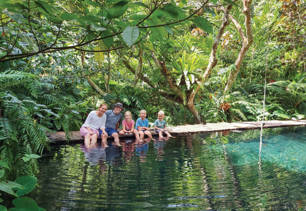 A photo of Vicki Cornish and her family sitting on a log above a pond.