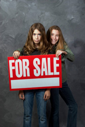 girl holding "for sale" sign in front of other girl
