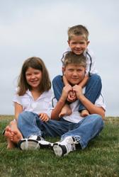 girl, boy, and younger boy sitting on grass