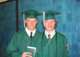 two teenage boys wearing graduation robes and smiling