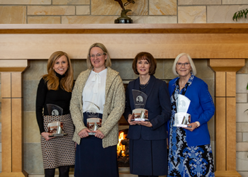 Four women standing together holding awards