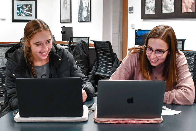 two girls smiling while being on the computer