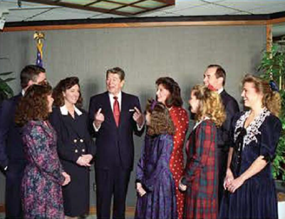 Three men, one being former president Ronald Regan, and five women are talking in a half circle