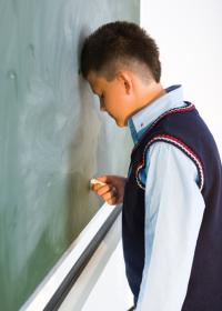 boy resting his forehead against a chalkboard