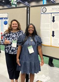 Presenters standing next to scholarly poster.